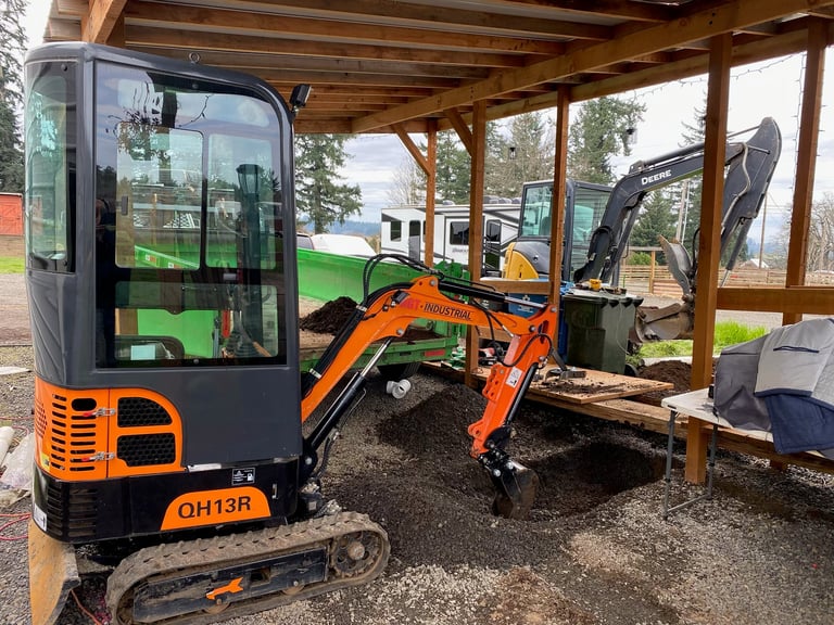 Orange and black mini excavator QH13R parked under wooden shelter with equipment