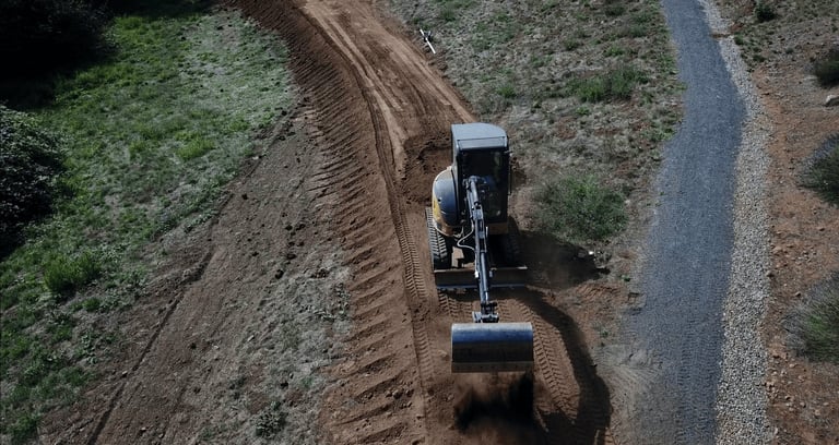 Overhead view of a road roller compacting freshly laid asphalt on a rural road surrounded by vegetation