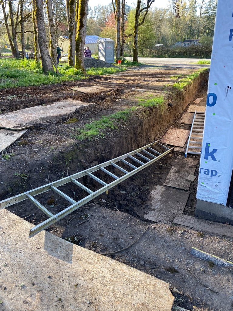 Metal ladder and ramp at entrance to blue trailer parked in wooded campground with excavated ground and grass