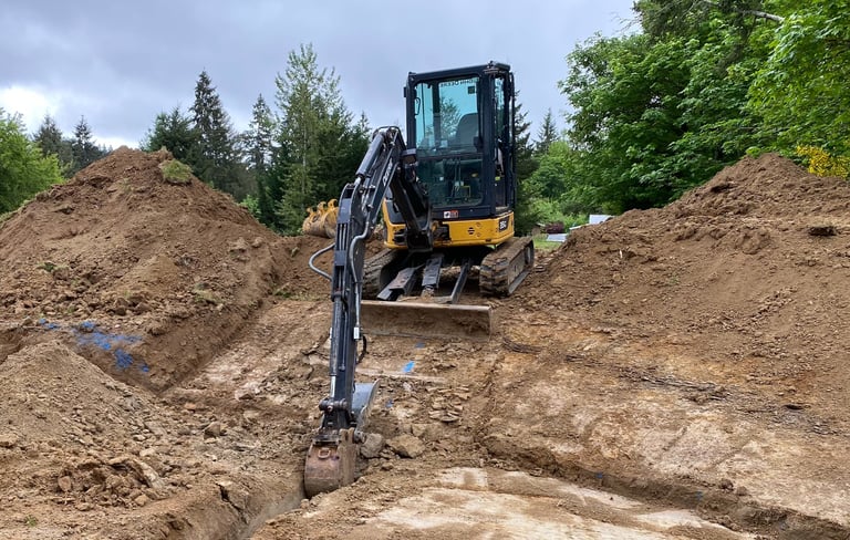 Black and yellow excavator digging in dirt pile surrounded by trees on construction site