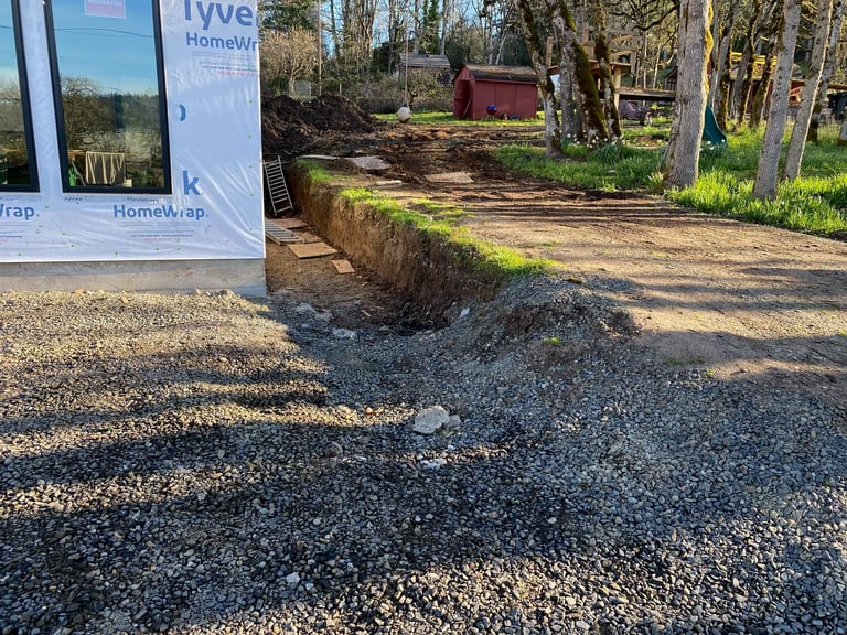 Gravel driveway with erosion damage and exposed edge, trees and red building in background