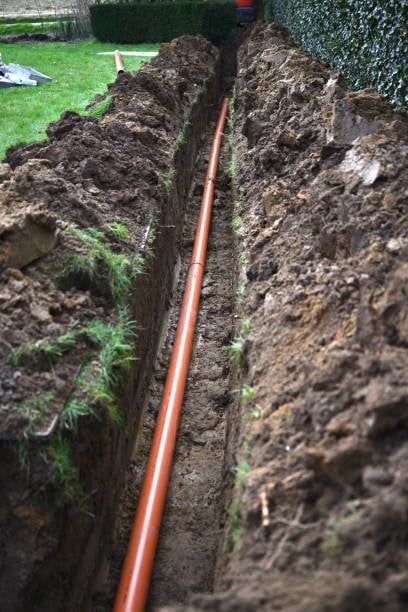 Orange PVC pipe laid in a deep trench with soil walls on both sides during underground utility installation
