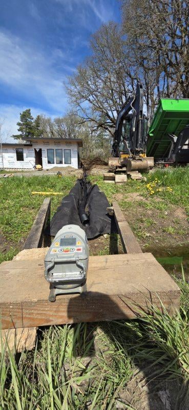 Farm equipment including an auger mounted on a trailer with green tractor and farm building visible in background